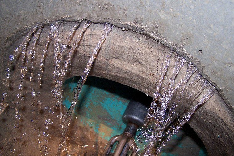 Groundwater streaming into a manhole through the joints in its concrete wall, over an instrument mounted below