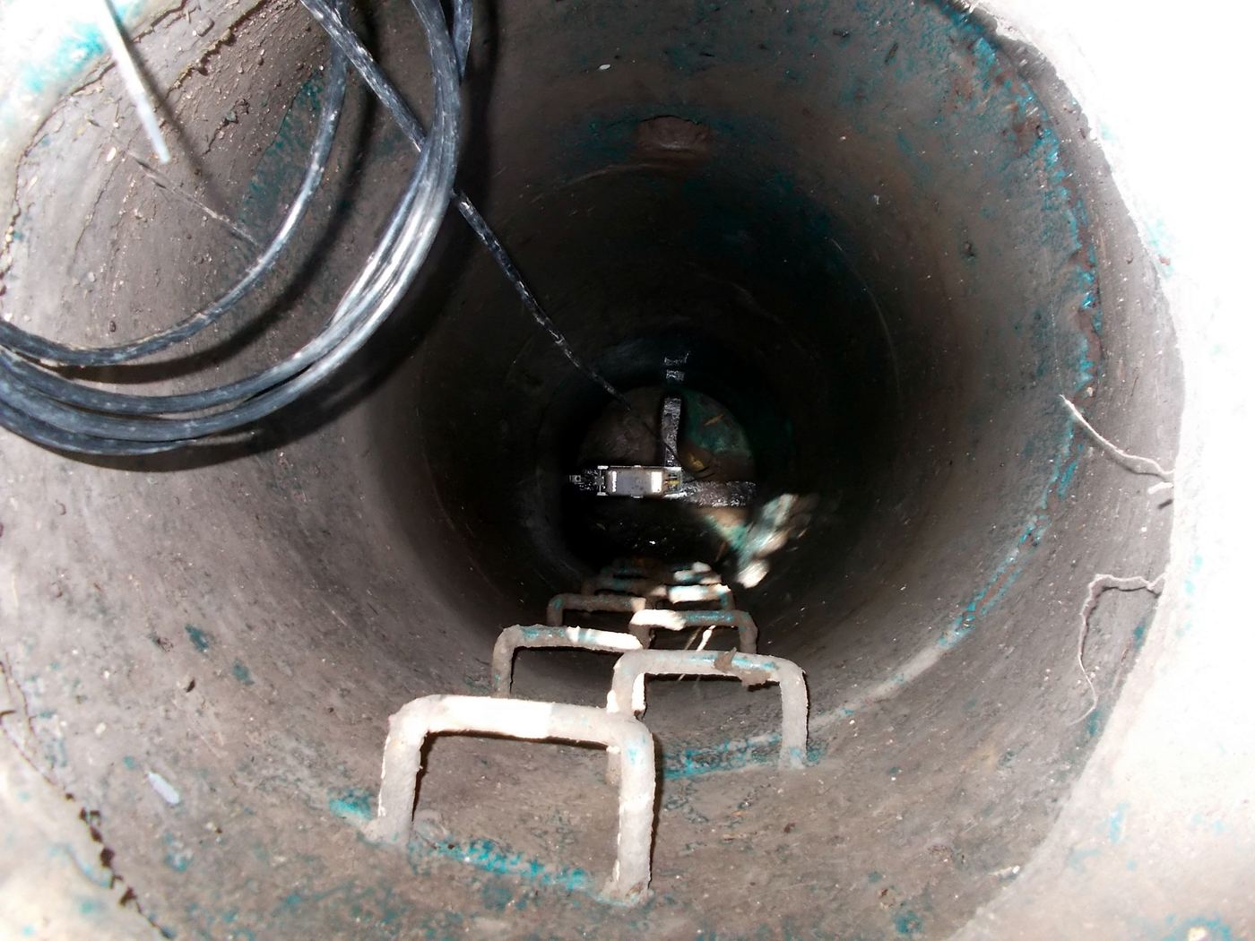 Looking down a manhole to a sensor bracket fixed across the invert of the pipe, with the sensor cable running up the shaft