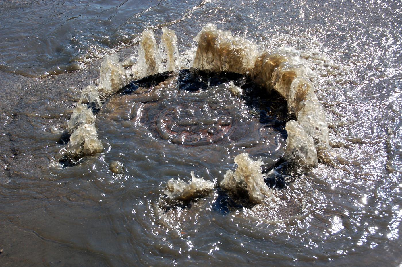 Wastewater surging up around a manhole cover and across a flooded street