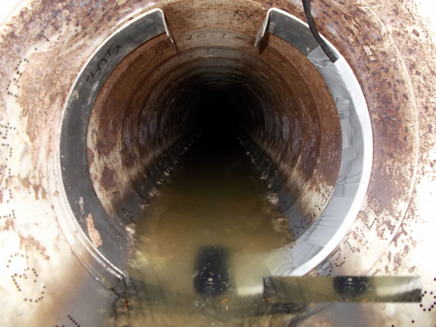 Looking along a large sewer pipe from a manhole, with the sensor mounting band fixed inside the entry and flow running away into the dark