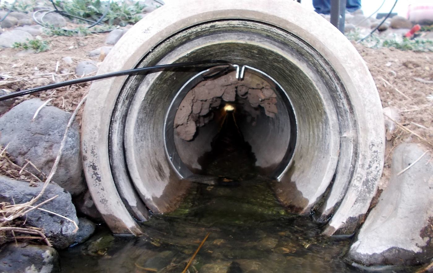 A sensor cable running into a concrete stormwater culvert with a shallow stream flowing out of it between rocks