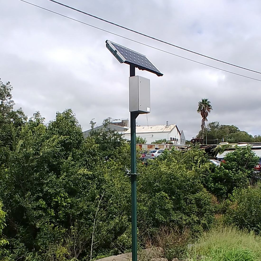 A solar panel and a telemetry enclosure mounted on a pole beside a monitoring site