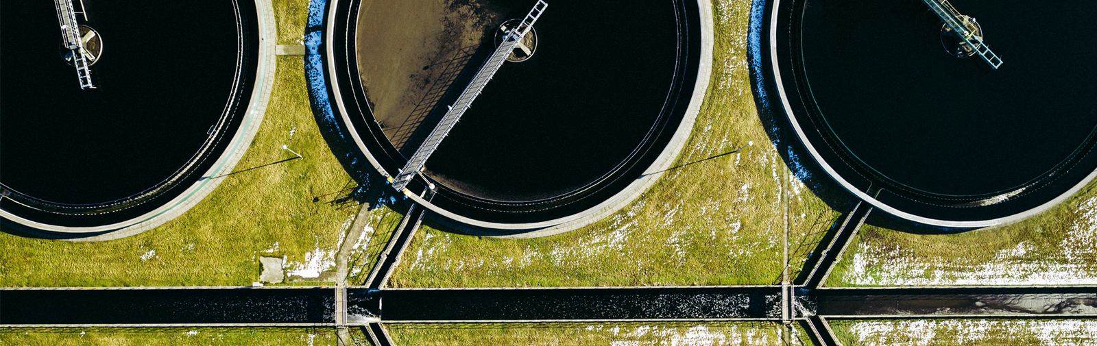 Aerial view of three circular clarifiers at a wastewater treatment plant, joined by walkways across the grass
