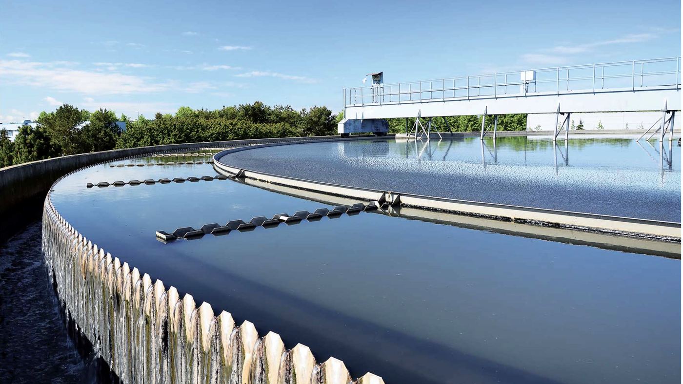 The circular clarifier of a wastewater treatment plant on a clear day, with its scraper bridge and weir